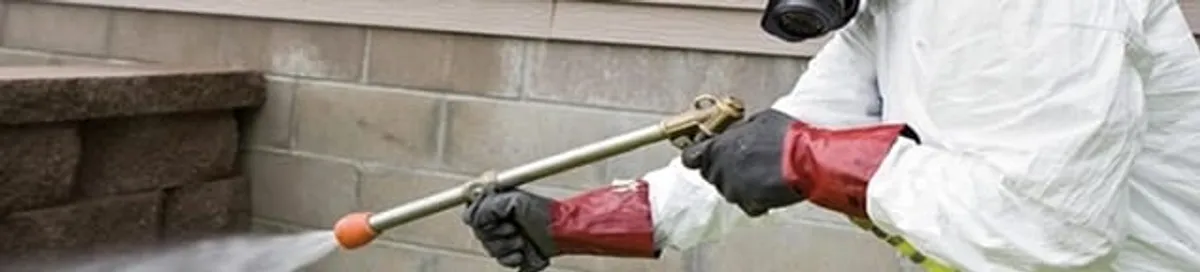 Pest control technician applying exterior insect treatment along a home foundation in Sacramento, CA