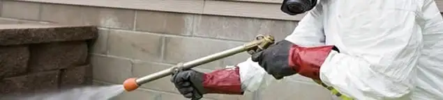 Pest control technician applying exterior insect treatment along a home foundation in Sacramento, CA