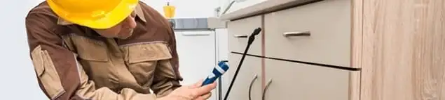 Roach exterminator applying treatment under kitchen cabinets in Sacramento, CA