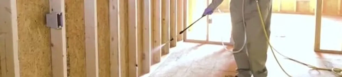 Termite treatment technician applying spray along framing and unfinished walls in Sacramento, CA