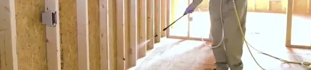 Termite treatment technician applying spray along framing and unfinished walls in Sacramento, CA